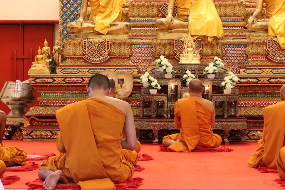 barbati purtand portocaliu in genunchi in fata lui Buddha